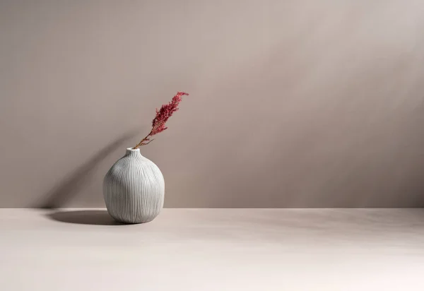 Minimalist still life scene. Ceramic ball-shaped vase and dried plants. Beige wall, sunlight, and long shadows on the background of the table. Trendy interior design. Copy space. Pastel colors