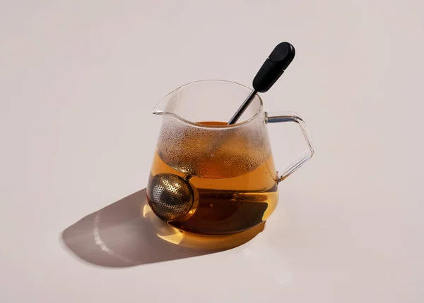 Tea and a tea strainer in a glass container on a beige background