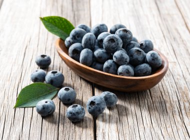 Çürük ve yaban mersini yaprakları eski bir tahta üzerinde. Arkadaki ahşap kasede yaban mersini..