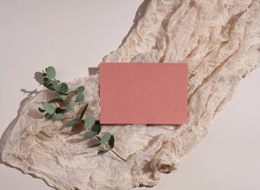 Yaz düğün kırtasiyesi modeli. Sade, turuncu tebrik kartı, davetiye, okaliptüs yaprakları ve bej arka planda sargı bezi. Doğal ışık ve gölge örtüsü. Düz yatış, üst görünüm.