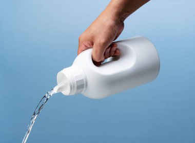 Şişeyi al ve deterjanı doldur. Mavi arka plan. Temizlik kavramı.