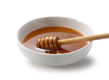 Manuka balı beyaz bir seramik kasede, içinde ahşap bir kepçe var, beyaz arka planda izole edilmiş.