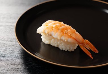 Özel ebi (karides) nigiri suşisini siyah bir tabakta koyu bir arka planda yakın plan.