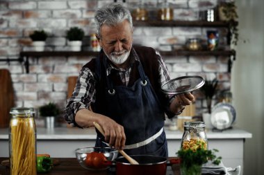 Son sınıf öğrencisi makarna için sos pişiriyor, tavada ahşap spatula kullanıyor.