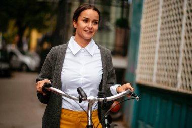 Gülümseyen bir kadın bisiklet tutuyor ve ileriye bakıyor. 