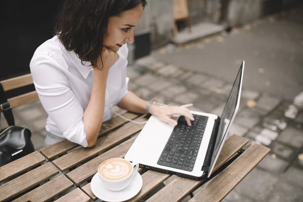 woman freelancer working with laptop at outdoor cafe with coffee cup