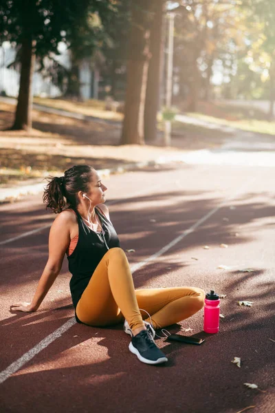 woman in sportive clothes sitting on running track listening music with earphones