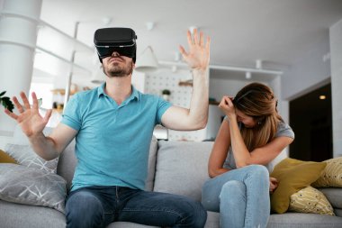 Mutlu çift oturma odasında sanal gerçeklik gözlükleriyle eğleniyor. Evde video oyunu oynayan ve eğlenen genç bir çift..