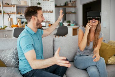 Mutlu çift oturma odasında sanal gerçeklik gözlükleriyle eğleniyor. Evde video oyunu oynayan ve eğlenen genç bir çift..