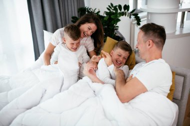 Genç bir aile yatakta eğleniyor. Oğulları yatakta dinlenen mutlu ebeveynler.