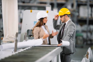 Fabrikadaki iş adamı ve iş kadını. Fabrika üretim hattında kalite kontrolde çalışan iki profesyonel insan..