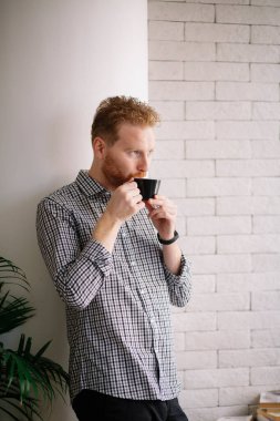 Kızıl saçlı yakışıklı işadamı ofiste kahve içiyor.