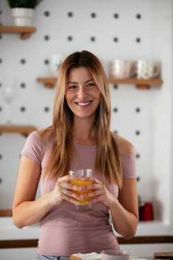 Güzel bir kadın mutfakta portakal suyu içiyor.
