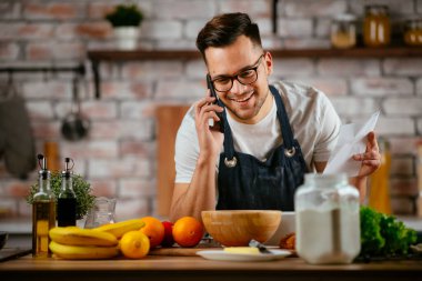 Yakışıklı adam mutfakta yemek pişiriyor ve cep telefonuyla konuşuyor..