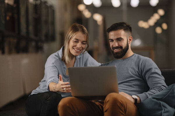 Happy businesswoman and businessman sitting on sofa and working on a laptop computer.