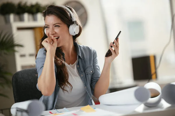 Young woman in office with headphones. Young casual businesswoman enjoying in her favorite song over headphones and singing while working on laptop in the office.