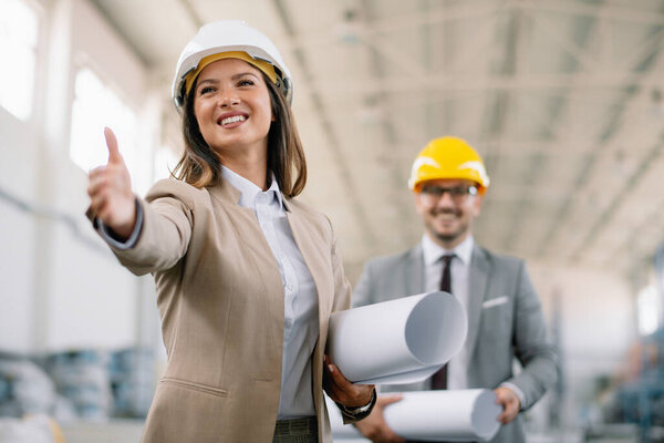 Smiling businesswoman handshaking with businessman on background. Beautiful architects in factory.