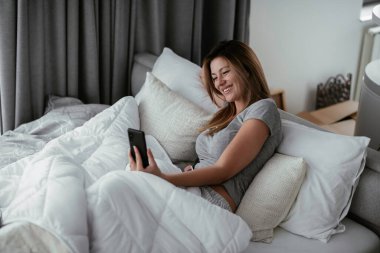 Yatakta telefon kullanan genç ve güzel bir kadın. Yatakta yatan kız..