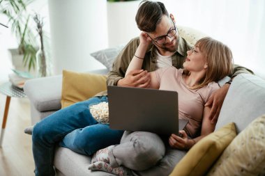 Dizüstü bilgisayarda film izleyen genç bir çift. Sevgili çift evde eğleniyor..