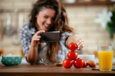 Yemek blogcusu fotoğraf çekmek için akıllı telefon kullanıyor. Mutfakta yemek fotoğrafı çeken genç bir kadın..