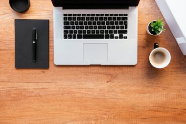 Ofis masasının en üst görüntüsü. Dizüstü bilgisayarlı ahşap masa, bir fincan kahve ve malzeme..