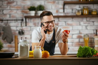Yakışıklı adam mutfakta yemek pişiriyor ve cep telefonuyla konuşuyor..