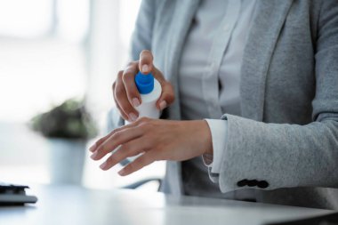 Gri takım elbiseli iş kadını ellerini ofiste dezenfekte ediyor.