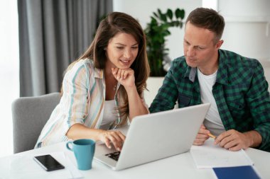 Erkek ve kadın evde dizüstü bilgisayar kullanarak çalışıyor.