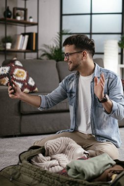 Giysilerini seyahat çantasına koyan gülümseyen genç adam. Yolculuğa hazırlanan adam.