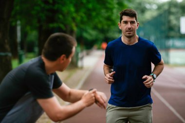 Gençler yarış pistinde antrenman yapıyor. İki genç arkadaş atletizm pistinde koşuyor.