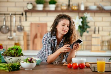 Yemek blogcusu fotoğraf çekmek için akıllı telefon kullanıyor. Mutfakta yemek fotoğrafı çeken genç bir kadın..