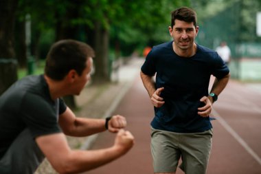 Gençler yarış pistinde antrenman yapıyor. İki genç arkadaş atletizm pistinde koşuyor.