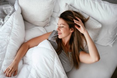 Uyandıktan sonra yatakta gerinen bir kadın. Güzel kız sabah güneşinin tadını çıkarıyor..