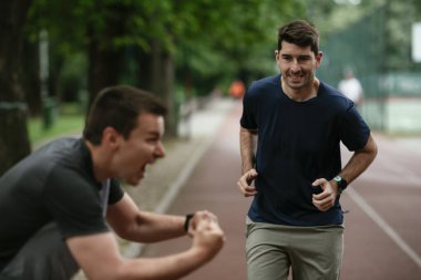 Gençler yarış pistinde antrenman yapıyor. İki genç arkadaş atletizm pistinde koşuyor.