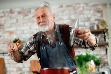 Yaşlı adam yemek yapıyor. Mutfakta kıdemli adam var..