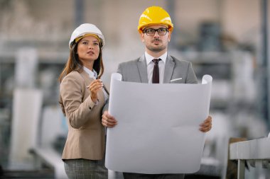 Miğferli kadın ve erkek mimarlar planları tartışıyor.