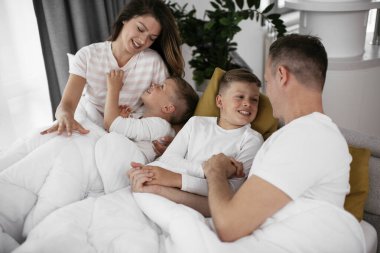 Genç bir aile yatakta eğleniyor. Oğulları yatakta dinlenen mutlu ebeveynler.