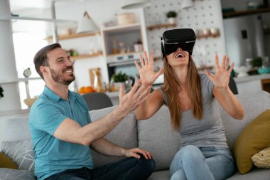 Mutlu çift oturma odasında sanal gerçeklik gözlükleriyle eğleniyor. Evde video oyunu oynayan ve eğlenen genç bir çift..