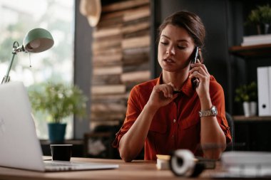 Telefon kullanan bir iş kadını. Ofiste telefonla konuşan mutlu genç bir kadın..