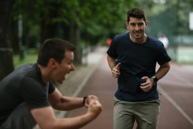 Gençler yarış pistinde antrenman yapıyor. İki genç arkadaş atletizm pistinde koşuyor.