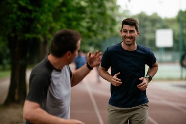 Gençler yarış pistinde antrenman yapıyor. İki genç arkadaş atletizm pistinde koşuyor.