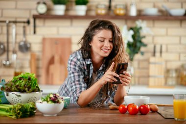 Yemek blogcusu fotoğraf çekmek için akıllı telefon kullanıyor. Mutfakta yemek fotoğrafı çeken genç bir kadın..