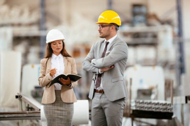 Miğferli kadın ve erkek mimarlar planları tartışıyor.