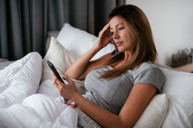 Yatakta telefon kullanan genç ve güzel bir kadın. Yatakta yatan kız..