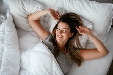 Uyandıktan sonra yatakta gerinen bir kadın. Güzel kız sabah güneşinin tadını çıkarıyor..