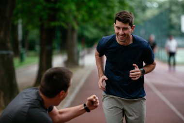Gençler yarış pistinde antrenman yapıyor. İki genç arkadaş atletizm pistinde koşuyor.