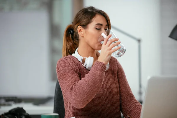 Dizüstü bilgisayarında çalışan ve su içen genç bir kadın.