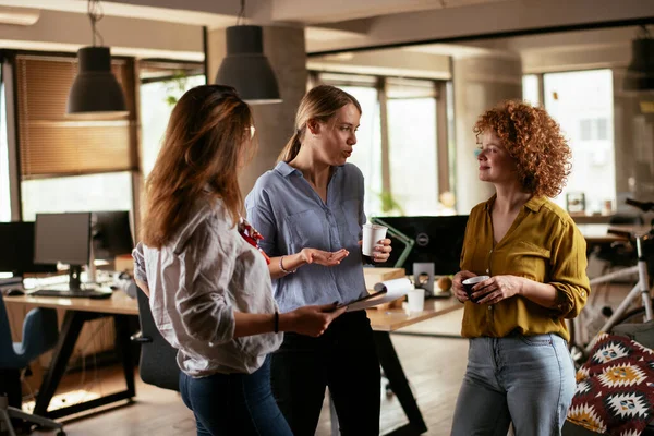 Girls talking and laughing in office. Beautiful women drinking coffee in the office