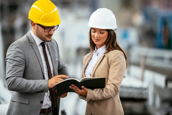 Miğferli kadın ve erkek mimarlar planları tartışıyor.