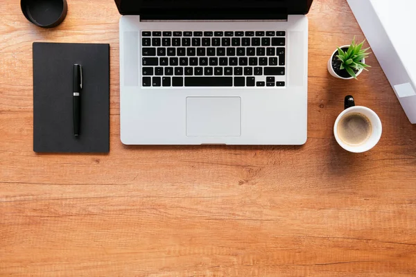 Ofis masasının en üst görüntüsü. Dizüstü bilgisayarlı ahşap masa, bir fincan kahve ve malzeme..